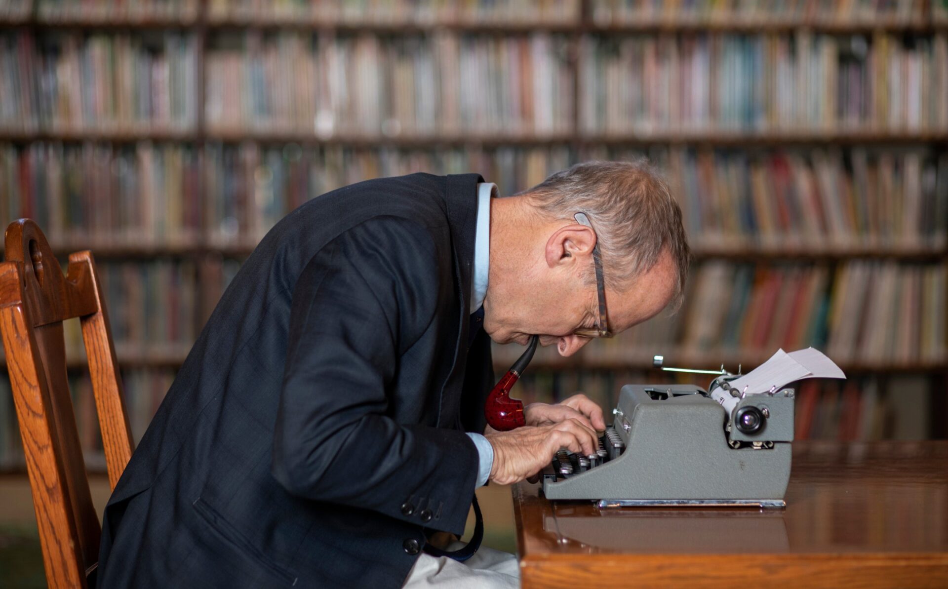 David Sedaris typing on a typewriter in front of bookshelves.