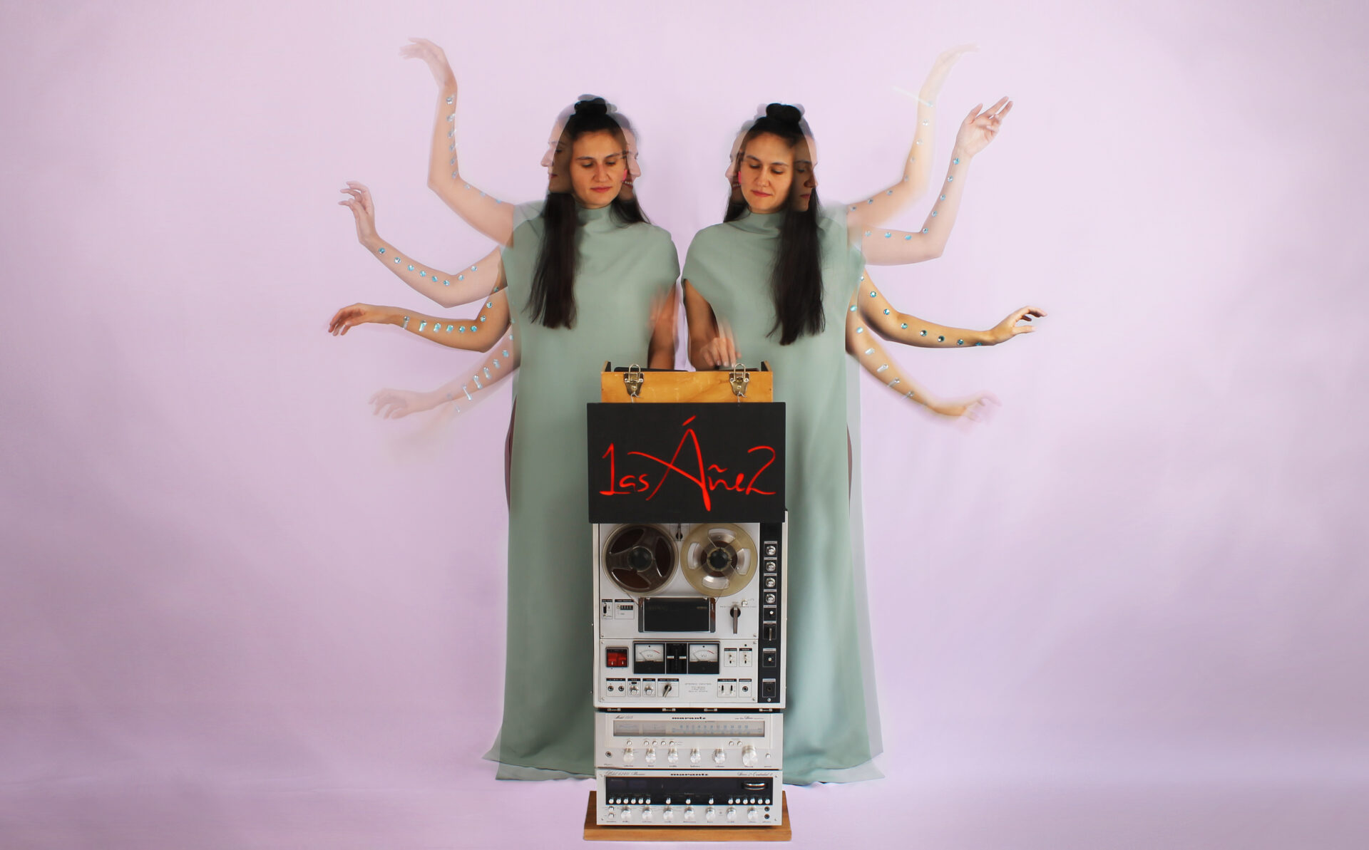 Las Áñez twin musicians performing beside a reel-to-reel tape machine against a soft pink background.